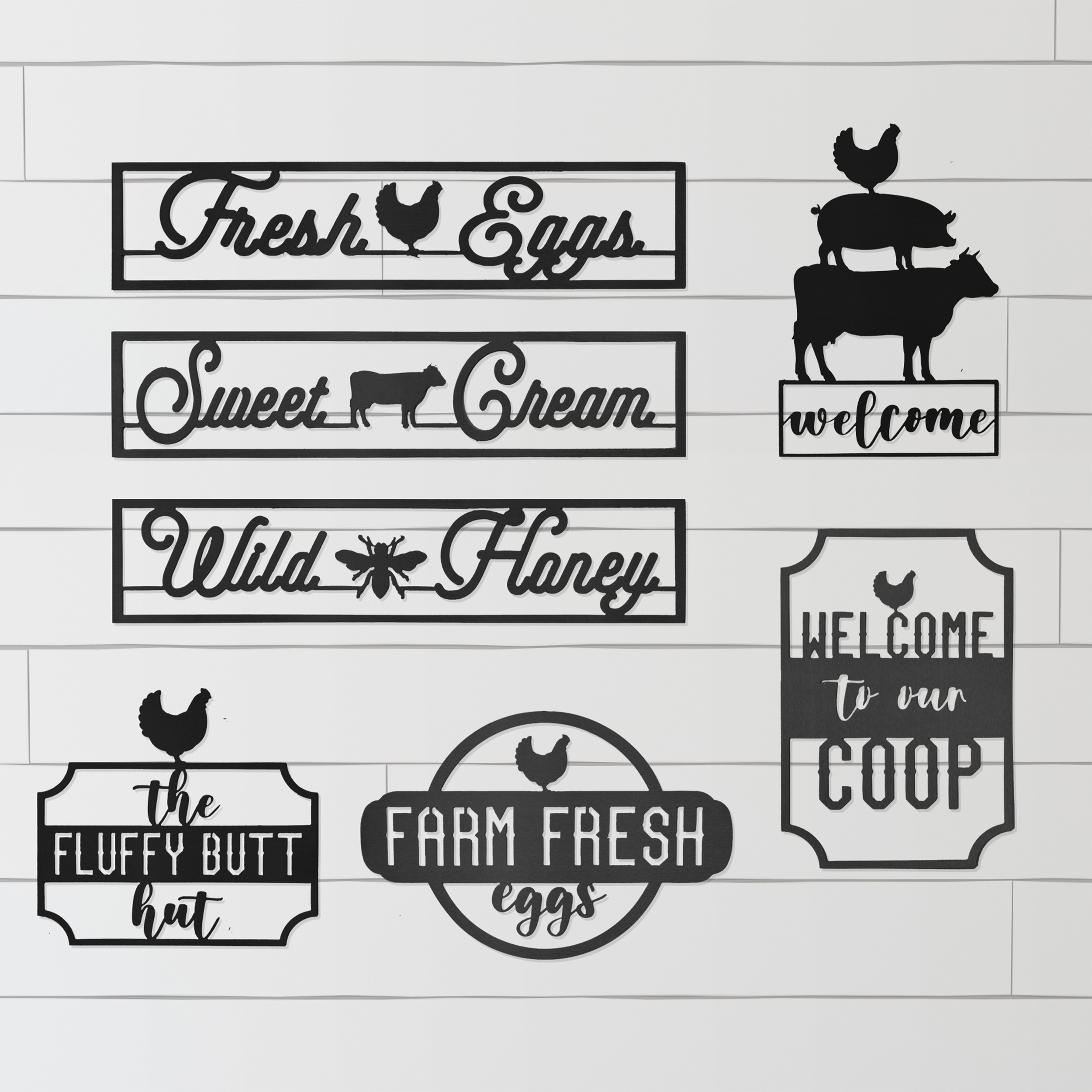 A collection of black metal wall signs with farm themes: \“Fresh Eggs\“ with a chicken, \“Sweet Cream\“ with a cow, \“Wild Honey\“ with a bee, a \“Welcome\“ sign featuring stacked animals, and humorous phrases like \“The Fluffy Butt Hut\“ and \“Welcome to our Coop,\“ some featuring chicken silhouettes.
