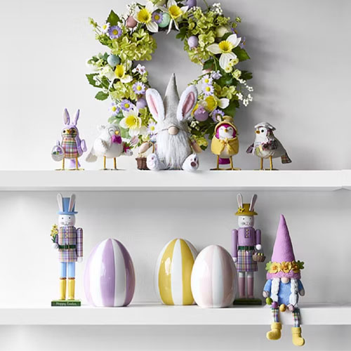 A decorative display with a floral wreath, a plush gnome, and assorted animal figurines on the upper shelf; the lower shelf has pastel-striped egg decorations and whimsical bunny figures.