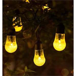 Outdoor string lights with glowing yellow bulbs hang among foliage.