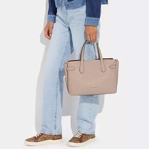 A person wearing blue jeans, a denim jacket, multi-colored sneakers, and holding a beige tote bag.
