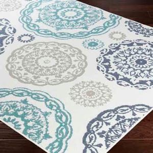 A Merriwood outdoor rug featuring circular, intricate patterns in teal, gray, and blue on a white background, placed on a dark wooden floor.