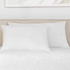 A bed features two large white pillows against a beige headboard, with white bedding and part of a decorative abstract print on the wall above.