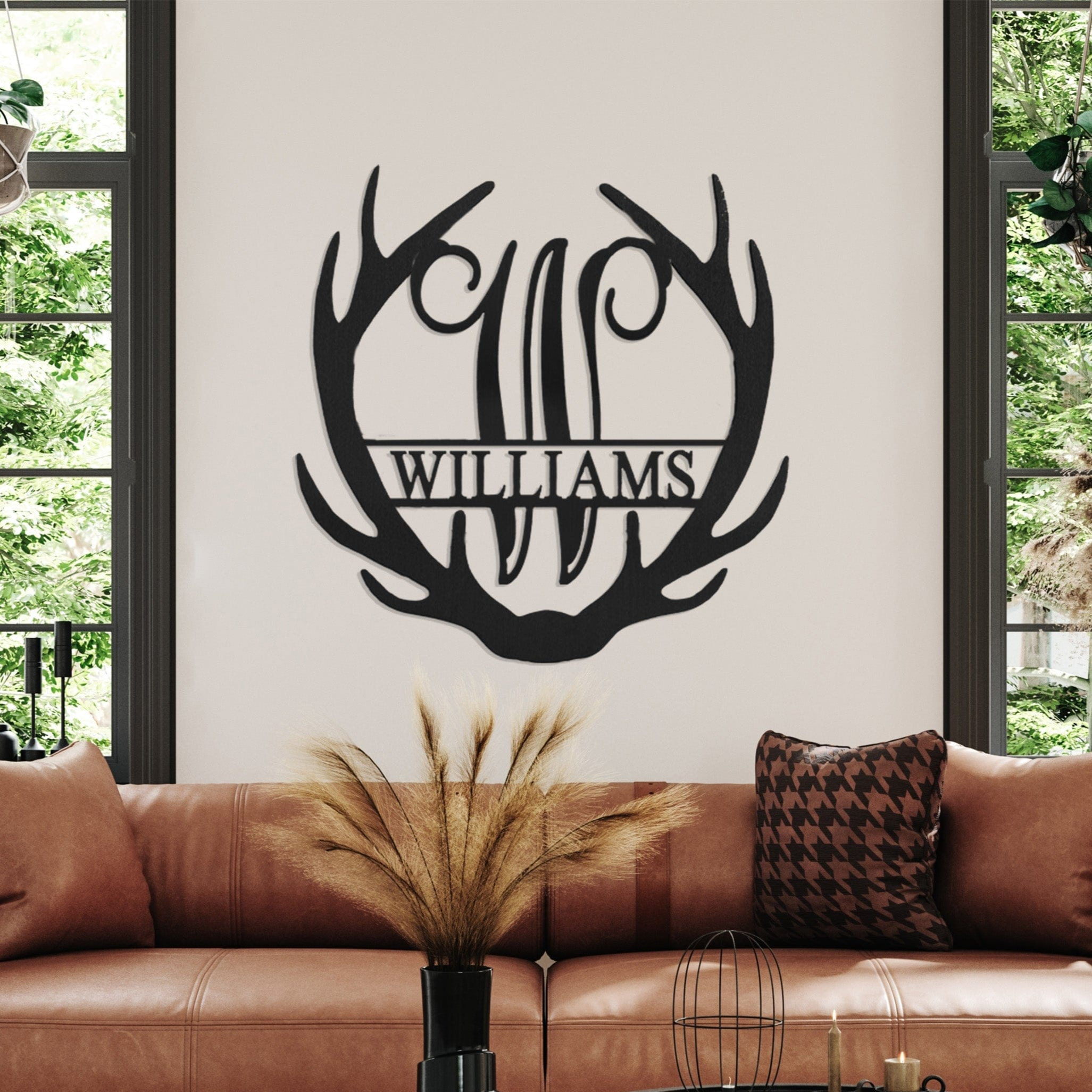 Wall art with an antler design and the name \“Williams\“ decorates a modern living room with a leather sofa, cushions, and round coffee tables.