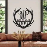 Wall art with an antler design and the name \“Williams\“ decorates a modern living room with a leather sofa, cushions, and round coffee tables.