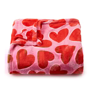A pink oversized plush throw blanket features red heart patterns, offering a soft and cozy texture.