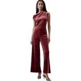 A woman is wearing a one-shoulder, maroon velvet jumpsuit with wide legs and paired with black high-heeled sandals.