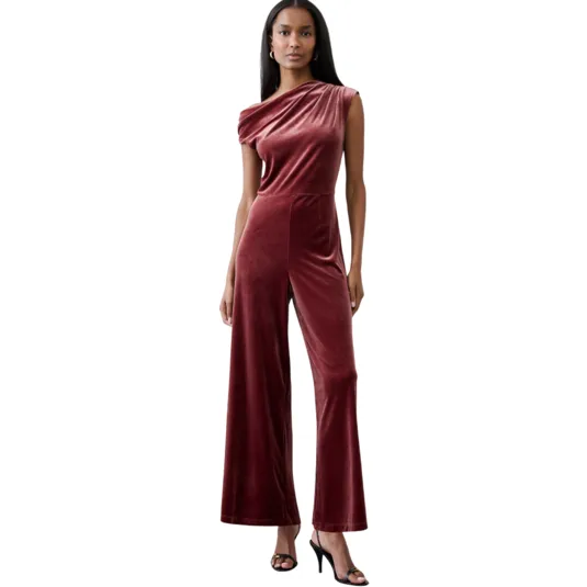 A woman is wearing a one-shoulder, maroon velvet jumpsuit with wide legs and paired with black high-heeled sandals.