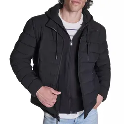 A man is wearing a black quilted puffer jacket with a hood and zipper, layered over a striped shirt and light blue jeans.