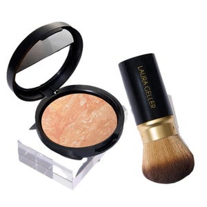 A compact of marbled powder with a mirror, paired with a gold-handled kabuki brush labeled \“LAURA GELLER.\“