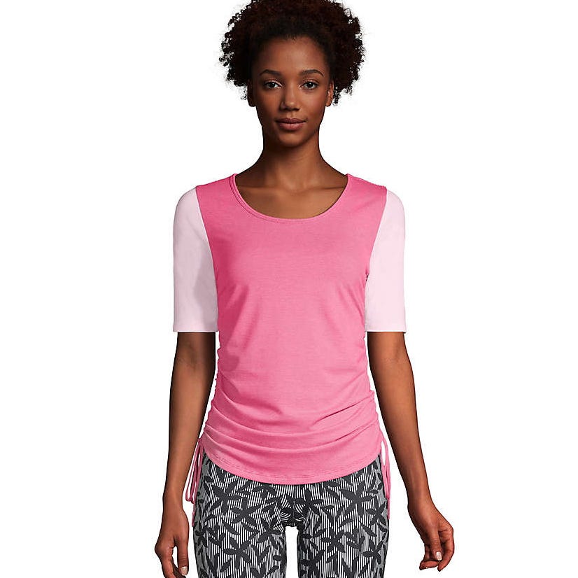 Pink drawstring top with short sleeves and a round neckline. The sides can be adjusted for a ruched effect. Paired with black and white patterned leggings.