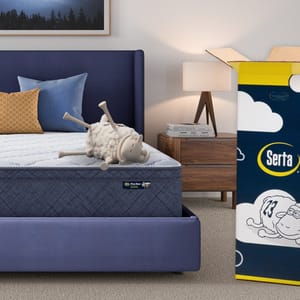A Serta mattress is displayed on a blue bed alongside a plush sheep toy, with a Serta-branded box next to it.