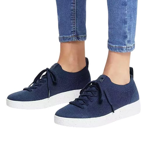 A pair of navy blue knit sneakers with white speckled soles and laces, worn with ankle-length blue jeans.