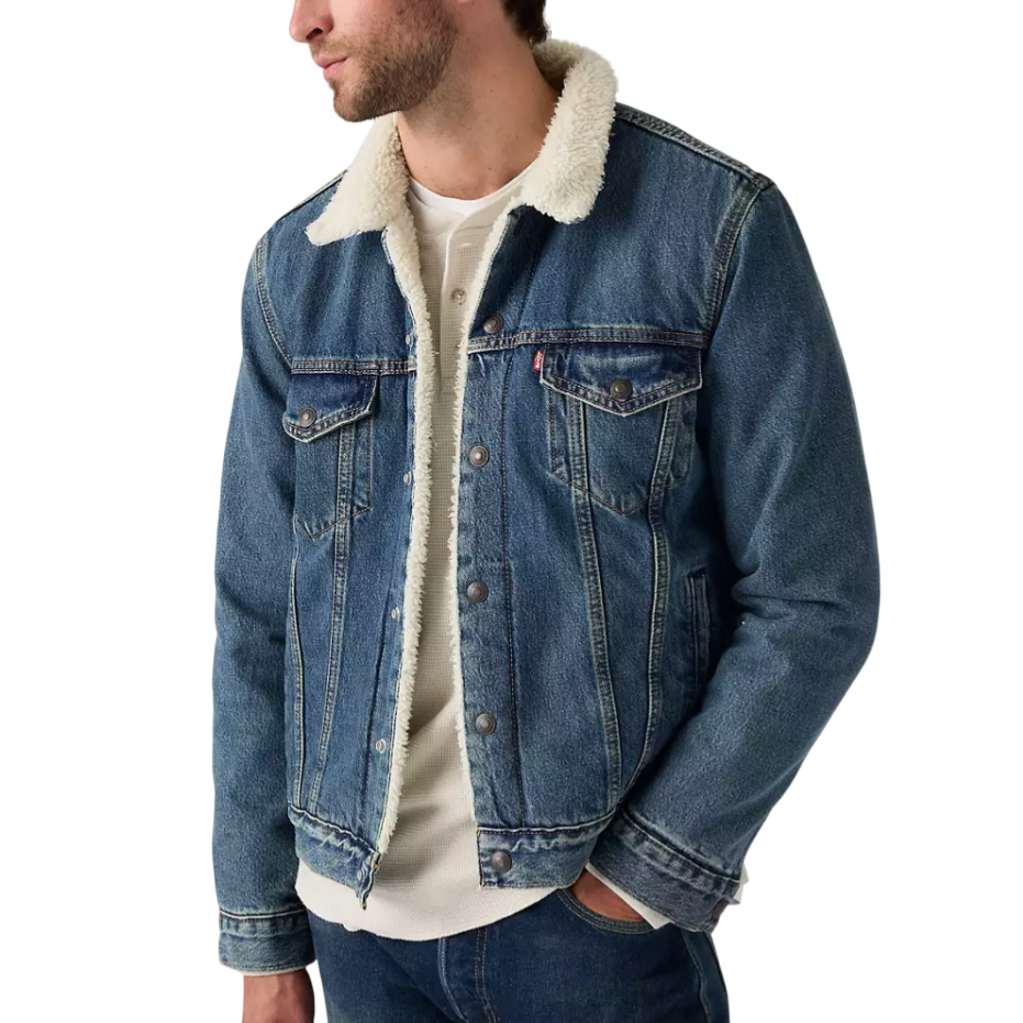 A man is wearing a blue denim jacket with a white shearling collar, paired with a white shirt and blue jeans.