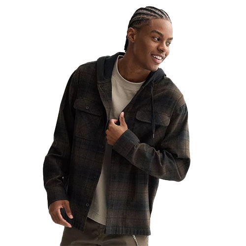 A man wears a dark plaid shacket with a hood, over a beige shirt, paired with olive pants. He has cornrow-style braids and is smiling, looking to the side.