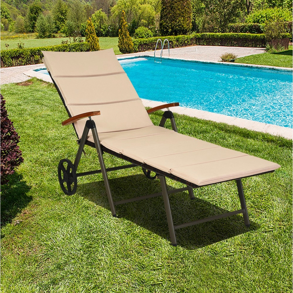 A reclining lounge chair with beige cushions, wooden armrests, and wheels on one end, placed on a green lawn beside a swimming pool.