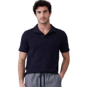 A man is wearing a dark-colored short-sleeve polo shirt and gray drawstring pants.