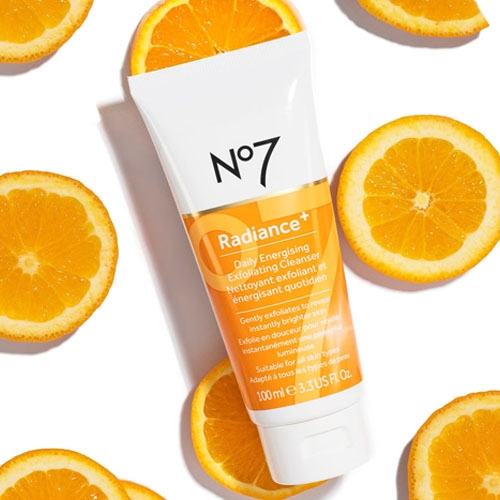 No7 Radiance+ Daily Energizing Exfoliating Cleanser tube with orange slices around it.