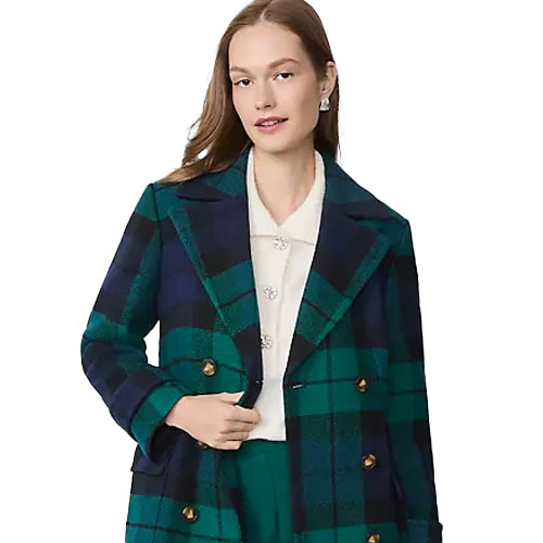 A model wearing a green and navy blue plaid coat over a white top with decorative buttons, paired with matching green pants.