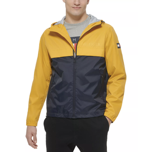A man wears a color-blocked jacket with a yellow top half and navy bottom half, featuring a hood and zip closure.