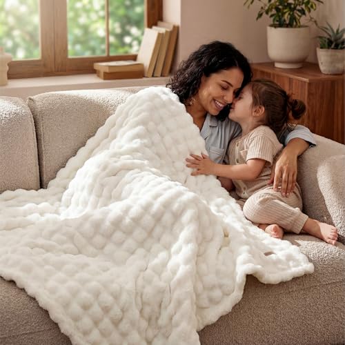 A woman and child are seated on a couch, enjoying time together under a fluffy, textured white blanket.