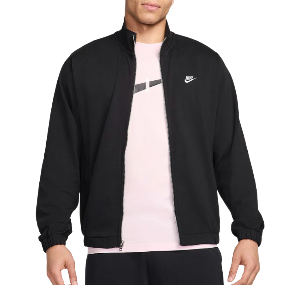 A person is wearing a black Nike jacket over a light pink t-shirt with a subtle design. The jacket features a small Nike logo on the left chest and has elastic cuffs.