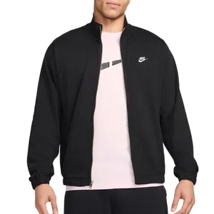 A person is wearing a black Nike jacket over a light pink t-shirt with a subtle design. The jacket features a small Nike logo on the left chest and has elastic cuffs.