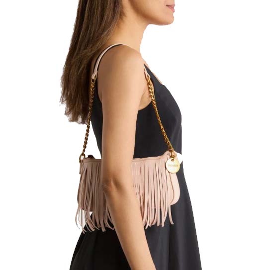 A woman wearing a sleeveless black dress carries a beige fringe handbag with a gold chain strap and a round gold charm.