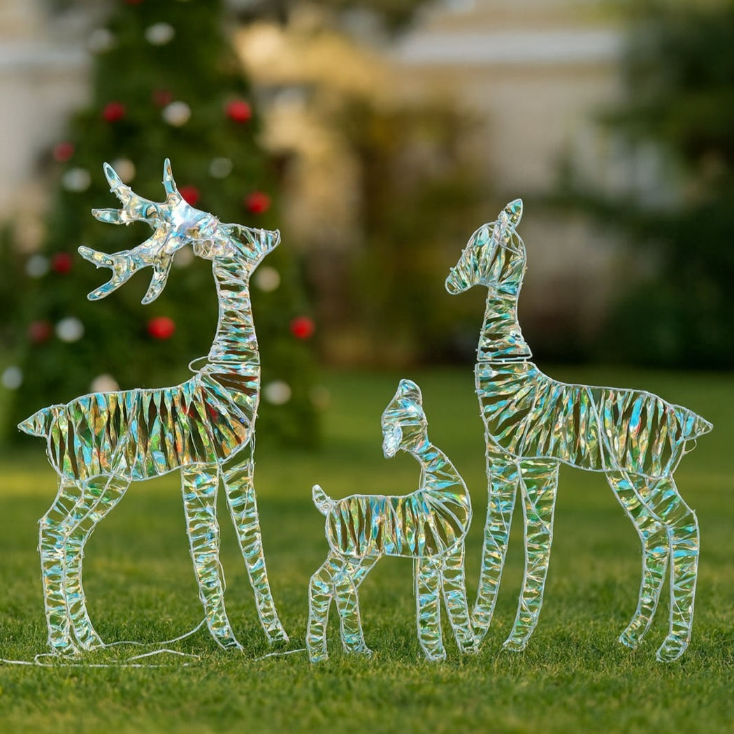 Three iridescent, deer-shaped decorations are displayed on a lawn, with a Christmas tree in the background.