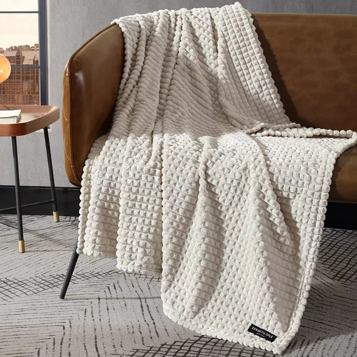 A textured white throw blanket is draped over a brown leather armchair next to a small round side table.