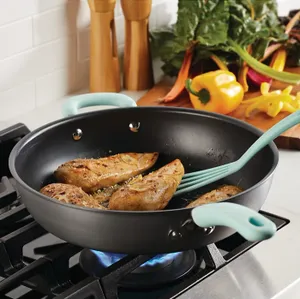 Non-stick frying pan with blue handles cooking chicken breasts on a gas stove, set against a backdrop of kitchen utensils and colorful vegetables.