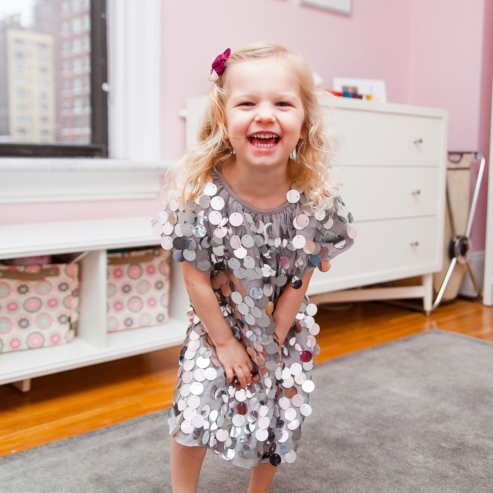 A young girl laughing, wearing a sequined dress and a hair clip.