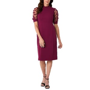 A knee-length, burgundy dress with short, sheer floral embroidered sleeves and a high neckline, paired with black strappy sandals.