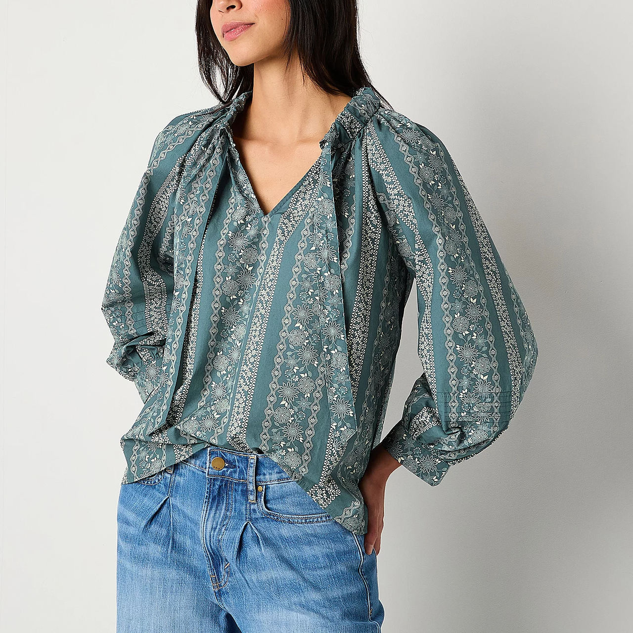 A woman is wearing a patterned teal blouse with voluminous sleeves paired with blue jeans.