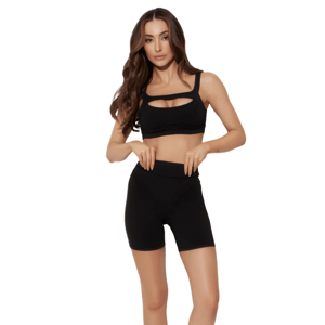 A woman in a black two-piece activewear set, featuring a sports bra with a cutout design and high-waisted shorts, paired with black athletic shoes, stands against a plain background.