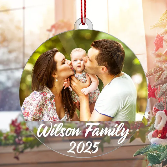A circular Christmas ornament features a family photo with a couple kissing their baby, labeled \“Wilson Family 2025.\“