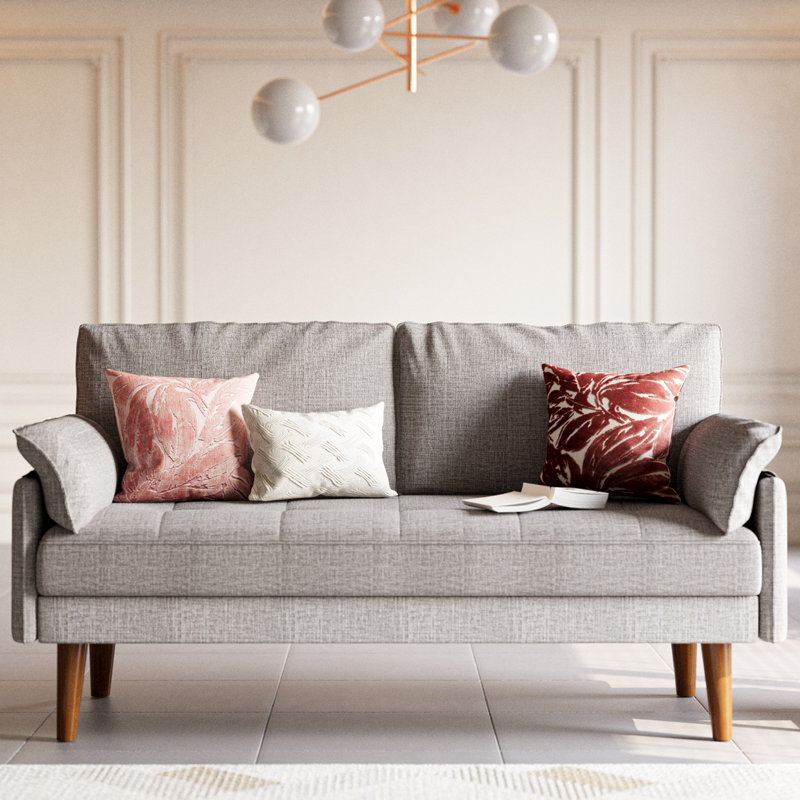 A 70\“ light gray upholstered sofa with wooden legs, featuring three decorative pillows in pink, white, and red. A book is open on the seat, and a modern chandelier with spherical lights hangs above.