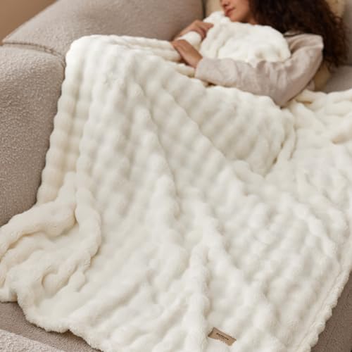A person is lying on a couch, covered with a fluffy white blanket featuring a textured design.