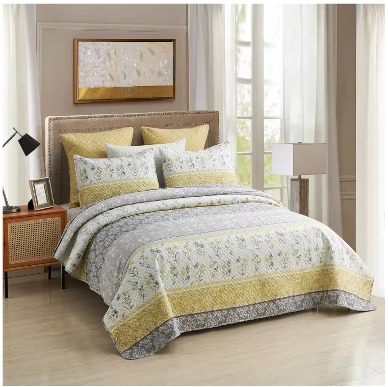 A 3-piece queen quilt set featuring a floral and geometric pattern in shades of gray and yellow, including one quilt and two matching pillow shams. The quilt has a border design and coordinates with warm-toned decorative pillows.