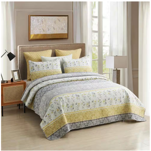 A 3-piece queen quilt set featuring a floral and geometric pattern in shades of gray and yellow, including one quilt and two matching pillow shams. The quilt has a border design and coordinates with warm-toned decorative pillows.
