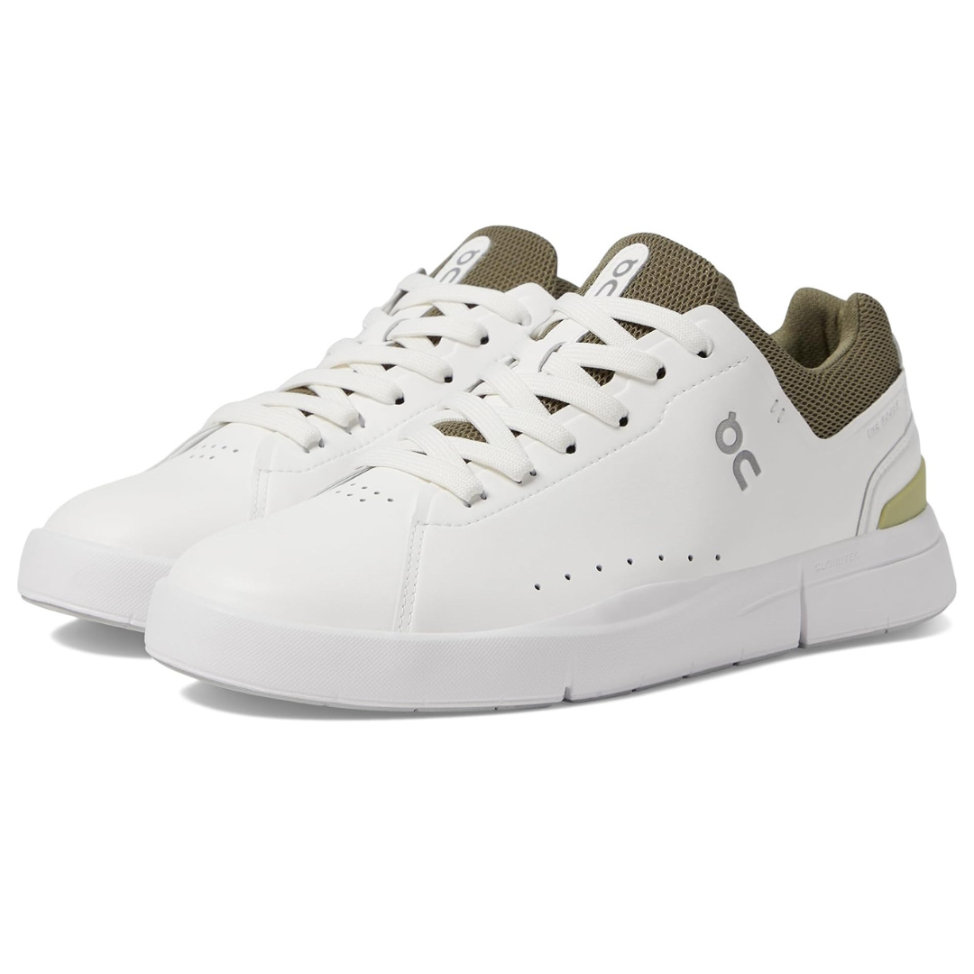 White low-top tennis sneakers with perforated detailing, featuring a smooth finish, white laces, and a contrasting olive-green interior lining and tongue. The shoes display a small \“OC\“ logo on the side.