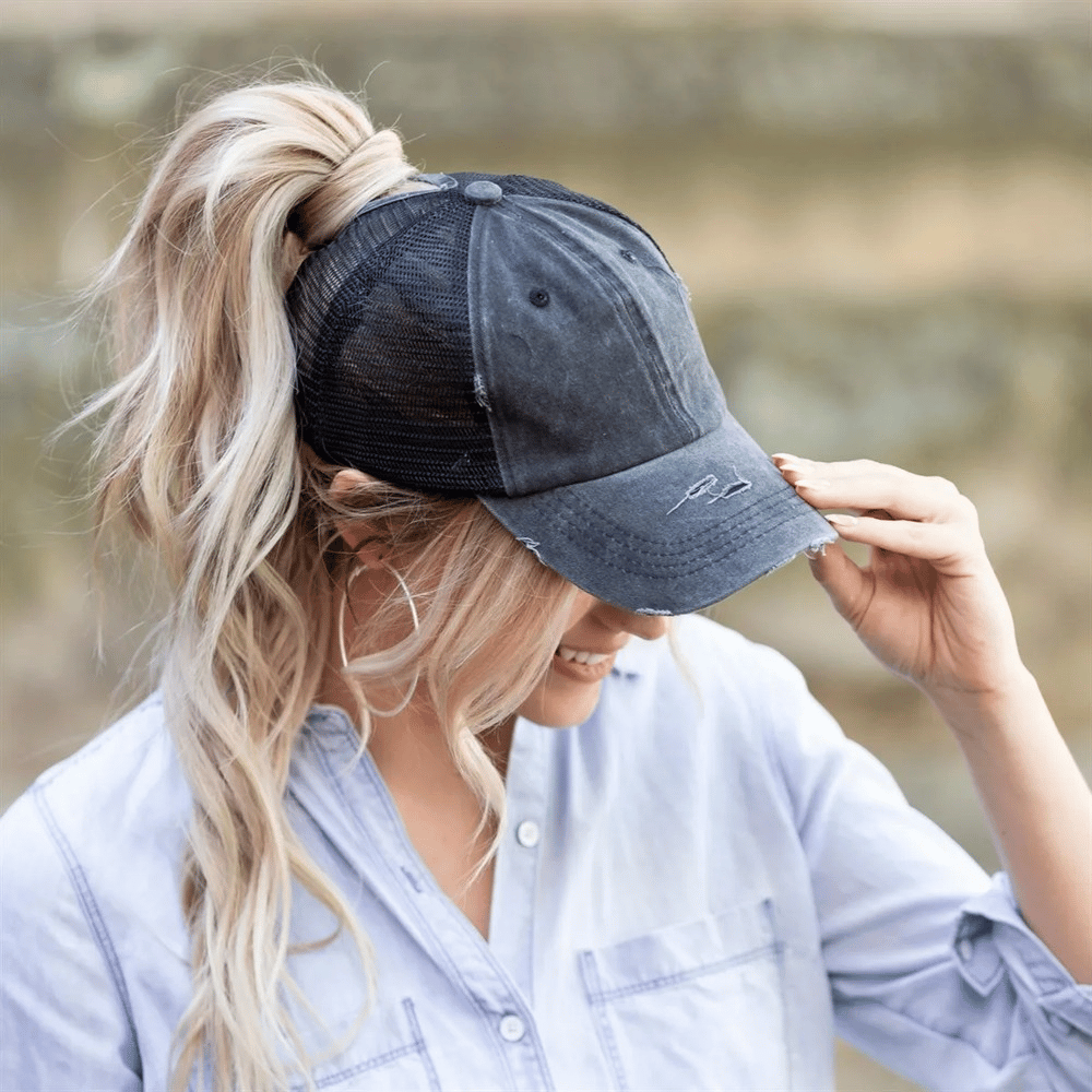 Two distressed ponytail hats, one showcased, featuring a mesh back design with an opening for a ponytail and a curved brim with a signature on the front.