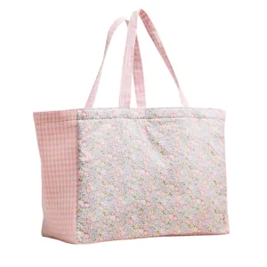 A pink tote bag with floral and checkered patterns, featuring two handles for carrying.