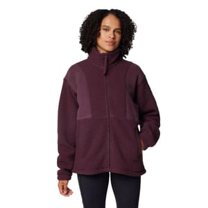 A woman is wearing a purple fleece jacket with a high collar and zip closure, featuring contrasting fabric panels on the shoulders.