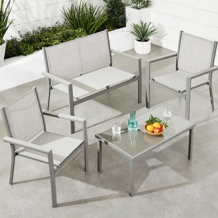 Outdoor patio set with two single chairs, a loveseat, and a glass-top coffee table. The furniture features a minimalist design with a grey metal frame and light grey fabric. The table holds a glass bottle, glasses, and a bowl of fruit.
