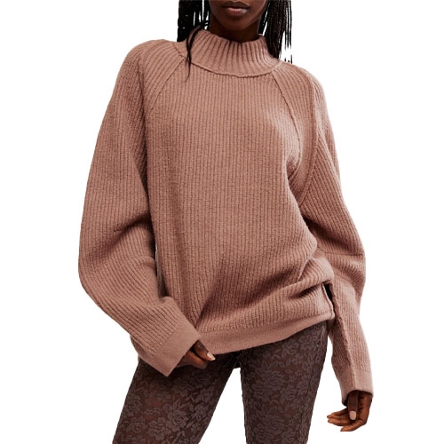 A person wearing a ribbed, oversized, dusty pink sweater with long sleeves and a high neckline, paired with dark patterned leggings.