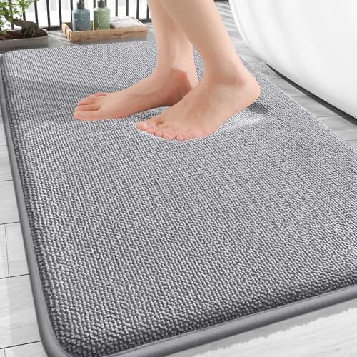 A person's feet are stepping onto a gray textured bath mat placed on a tiled floor next to a bathtub.