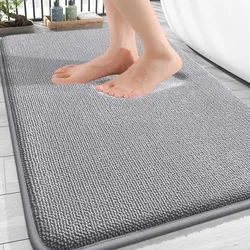 A person's feet are stepping onto a gray textured bath mat placed on a tiled floor next to a bathtub.