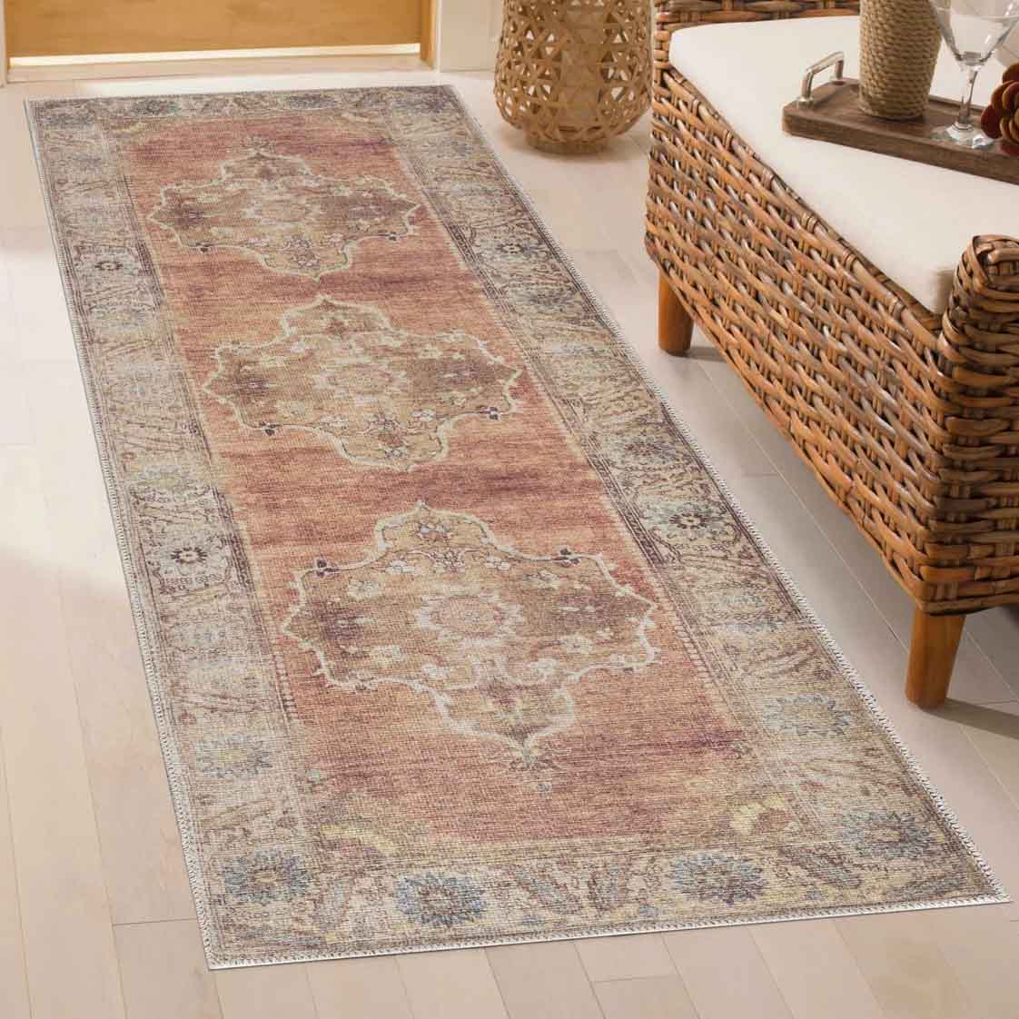 A decorative runner rug with a vintage design features intricate patterns in earthy tones, placed on a light hardwood floor next to a wicker sofa.