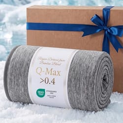 A gray bamboo blend blanket labeled \“Q-Max >0.4\“ with OEKO-TEX certification is rolled up on a snowy surface next to a brown gift box tied with a blue ribbon.