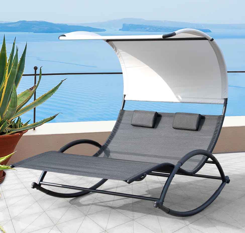 A double lounge chair with a curved frame and canopy, featuring two headrests, set on a terrace overlooking a body of water, accompanied by a potted plant.